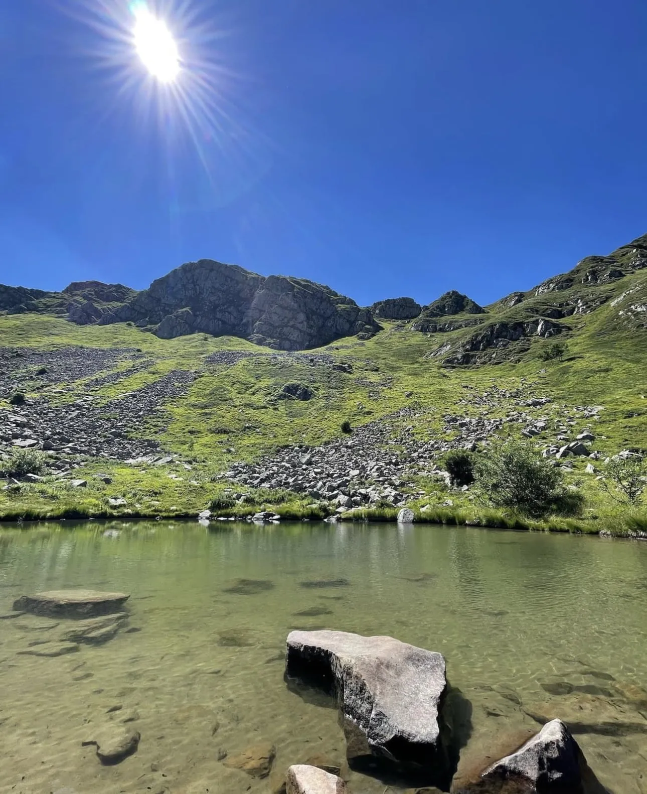 Helder bergmeer met stenen in het water en een rotsige bergkam erachter
