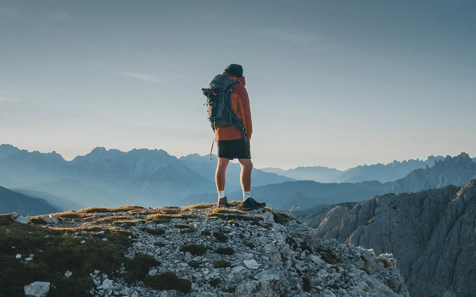 Wandelaar met rugzak op een rotsige bergtop kijkt uit over de bergketens