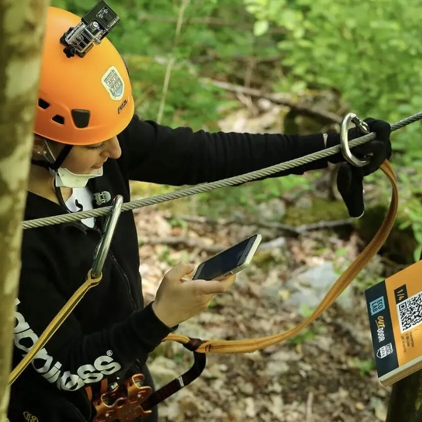 Deelnemer met helm en klimgordel bij een staalkabel in het bos