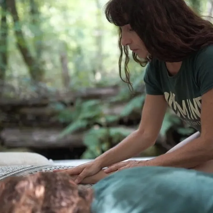 Behandelaar met de handen op de rug van iemand die op een mat in het bos ligt
